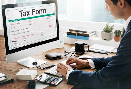 Businessman working on a computer while reviewing a tax form at an office desk