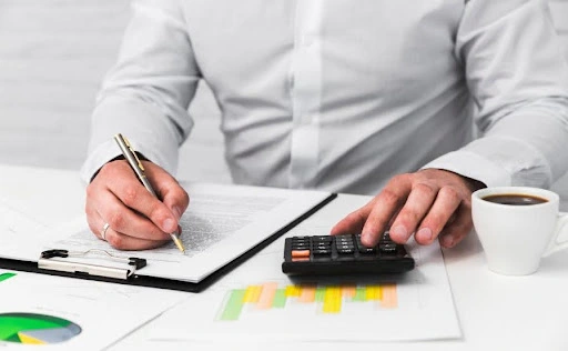 Person calculating financial figures while reviewing documents at a desk