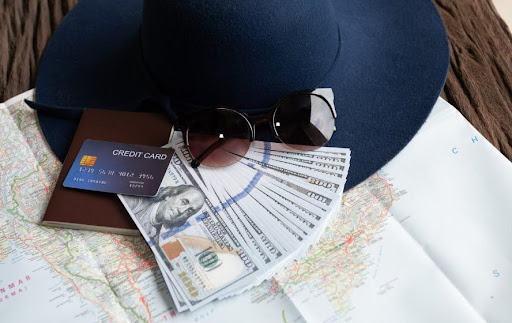 Travel essentials including cash, credit card, sunglasses, and a hat placed on a world map