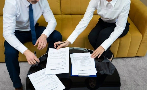 Two professionals sitting on a sofa reviewing and signing difc free zone business documents on a table
