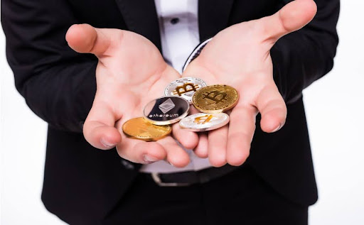 A professional in a dark suit holding several physical representations of cryptocurrency coins, including gold and silver Bitcoin and Ethereum, in their cupped hands