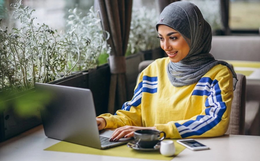 Arabian woman in hijab inside a cafe working on laptop