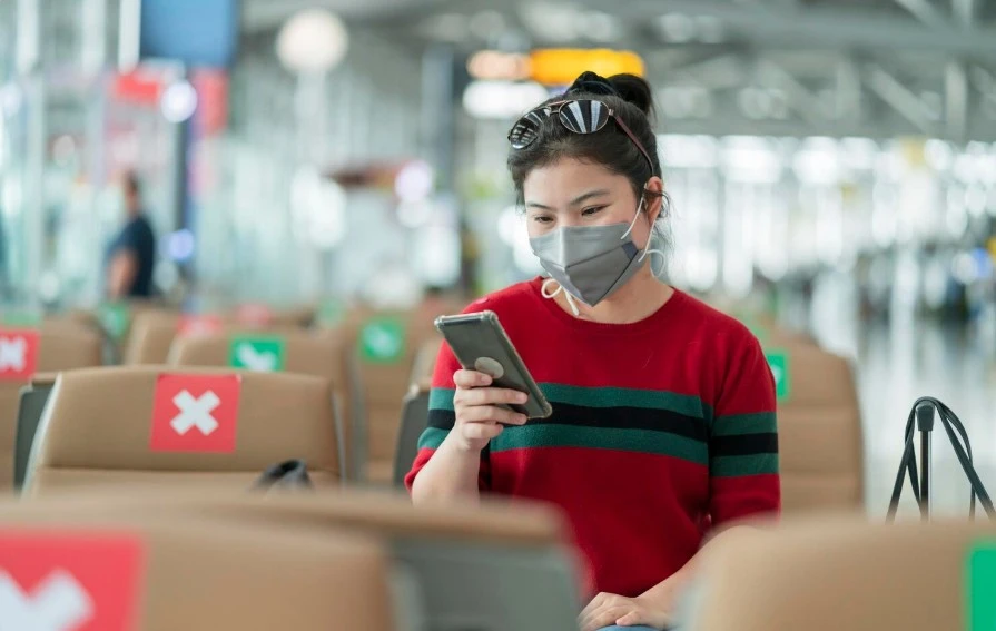 Young asian adult traveller wearing face mask hand hold smartphone